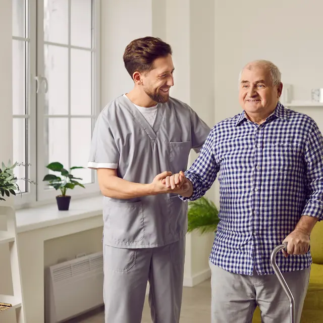 Caregiver helping a smiling senior man walk at home