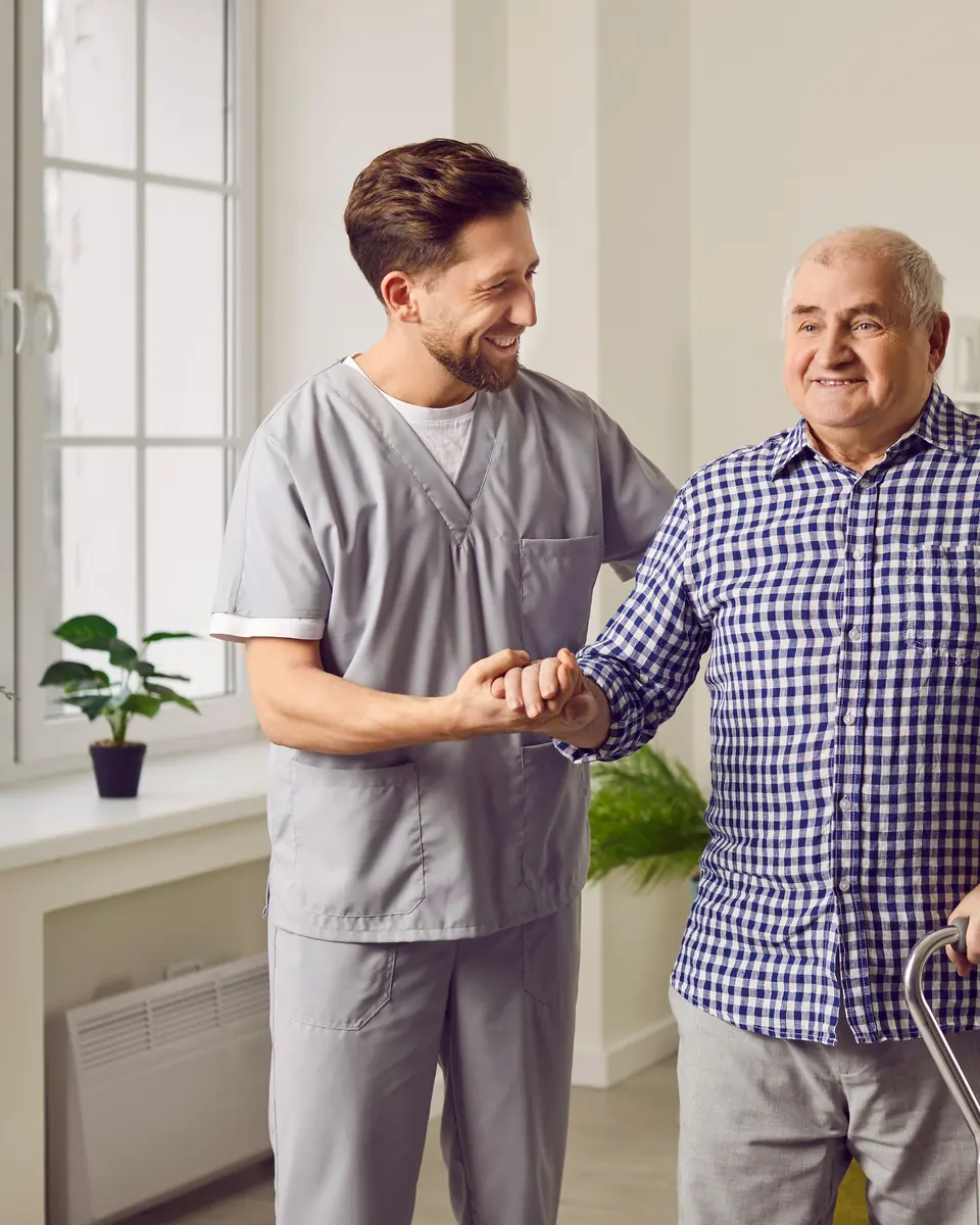 Caregiver supporting an older man walking with a cane in his Homewood home