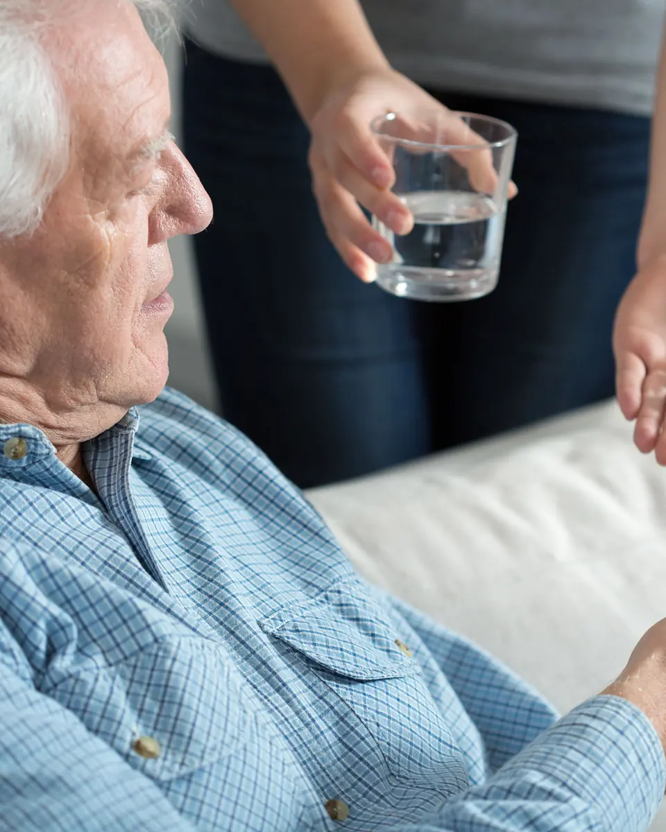 Caregiver bringing a glass of water to a senior man