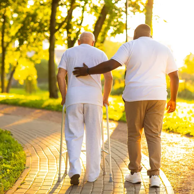 Caregiver walking with a senior man on a sunny path