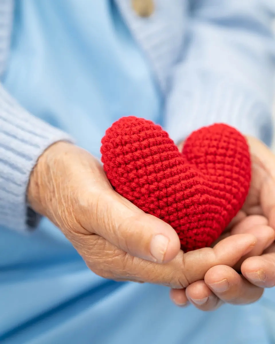 Senior hands holding a small red knitted heart