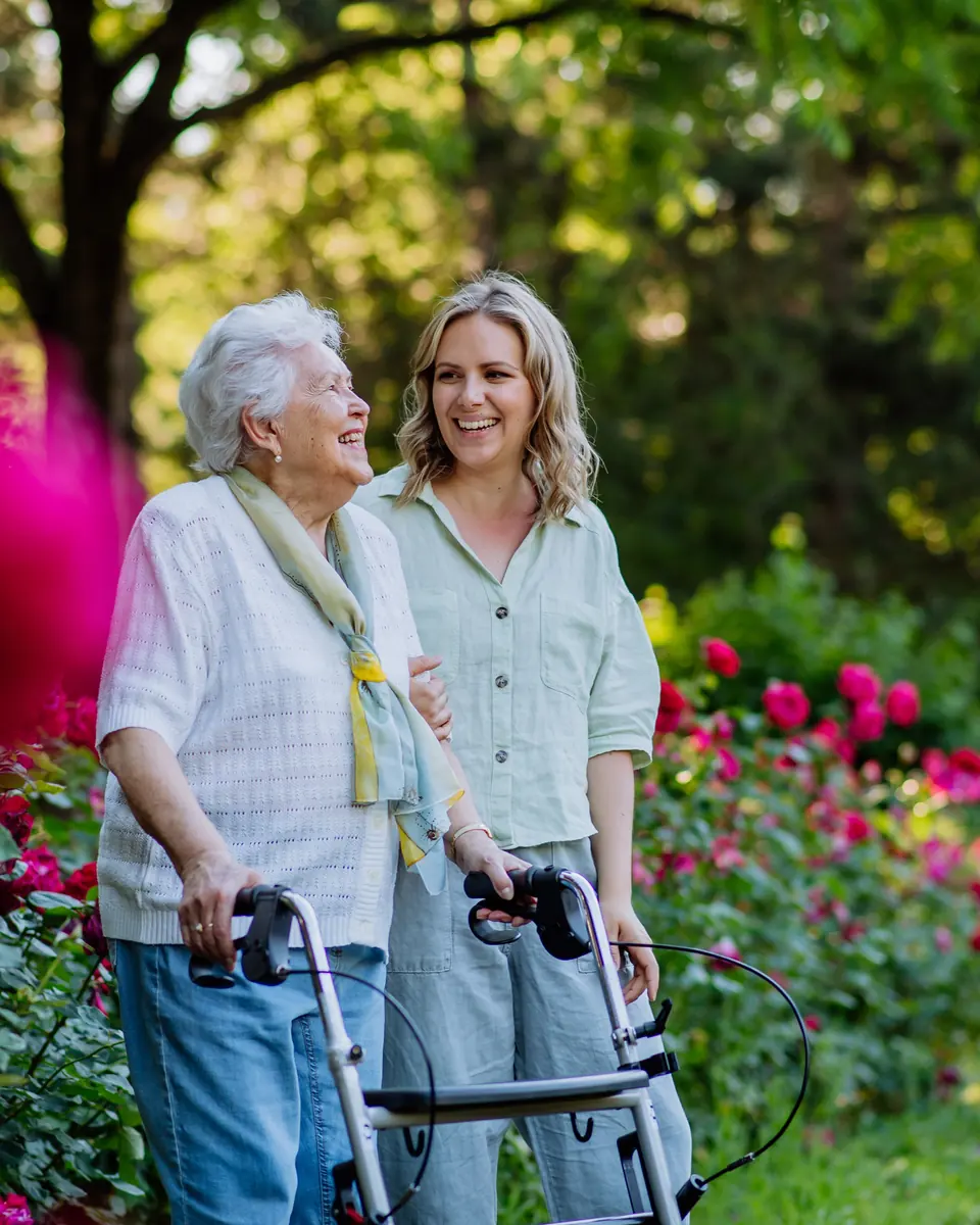 Senior woman laughing with her caregiver in a garden